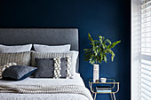 Double bed with grey headboard against petrol-blue wall
