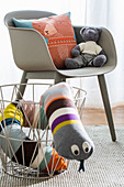 Fabric snake in metal basket next to grey shell chair in child's bedroom