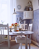 Shabby-chic dining table and chairs in front of blue-and-white wall with patina