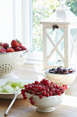 Summer fruits in bowls and colander on windowsill