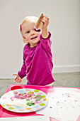 Kleines Mädchen stempelt mit Papprolle bunte Farbherzen auf Papier