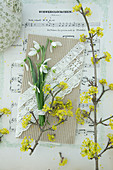 Schneeglöckchen auf DIY-Grußkarte mit Spitzenband und Zweig von Kornelkirsche auf Notenblatt