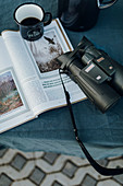 Binoculars, coffee in enamel cup and open magazine
