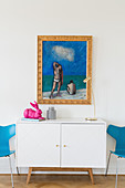 Blue painting with gilt frame above modern white sideboard