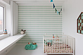 Kinderzimmer mit Rauten-Tapete, weißem Babybett und Regal