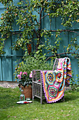 Multi-coloured crocheted blanket on chair on lawn in garden