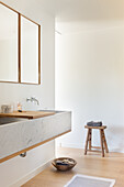 Waschtisch mit Marmorplatte und Holzhocker im minimalistischen Badezimmer