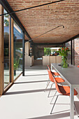 Heller Wohnraum mit Glasfront, Ziegeldecke und orangefarbenen Stühlen