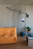 Oranges Klappsofa und schwenkbare Wandleuchte im minimalistischen Wohnzimmer