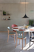 Modern dining area with round table, various chairs and concrete wall
