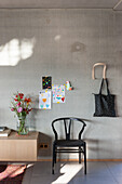 Exposed concrete wall with children's drawings, black wooden chair and sideboard