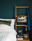 Bed with white bed linen and ladder used as magazine rack against petrol-blue wall