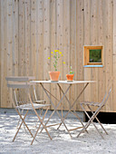 Gartentisch und Stühle aus Metall vor einer Hauswand mit hellem Holz