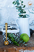 Eucalyptus branches in jug, Christmas baubles in fabric back and green apples
