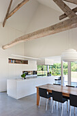 Moderne Küche mit Holzbalken, weißer Einrichtung und offenem Essbereich