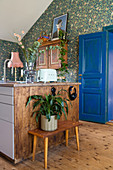 Houseplant on bench next to island counter in front of floral wallpaper