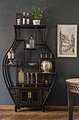 Black, vase-shaped shelving unit against dark grey wall in dining room