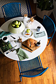 Zum schlichten Frühstück gedeckter Tisch mit blauen Stühlen