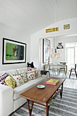 Retro coffee table in front of sofa with colourful scatter cushions in open-plan interior