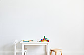 Weißer Kindertisch mit bunten Malstiften und Bauklötzen, weißer Stuhl und Hocker