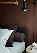 Bed with pillows and bolster against brown wall