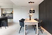 Wooden table and black chairs in modern dining area with kitchen in the background