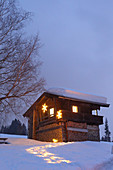 Beleuchteter Weg im Schnee zur alpinen Hütte am Abend