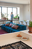 Living room with blue sofa, plants by the window and person in the background