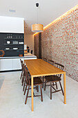 Wooden dining table and dark chairs, brick wall in modern eat-in kitchen