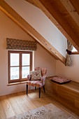 Armchair next to wooden bench below sloping ceiling in farmhouse