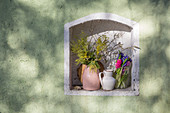 Vases of mimosa, hyacinths and hazel branches in niche in green wall
