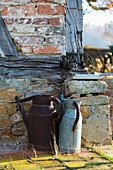 Old, rusty metal watering cans against weathered, half-timbered wall