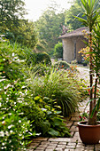 Gepflasterter Gartenweg im ländlichen, französischen Garten mit offener Scheune