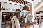 Large, metal pendant lamps above wooden dining table with stairway in background