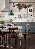 Pans hanging from rack above kitchen counter with grey cabinets and antique table in dining area