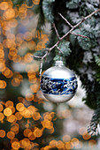 Silver-and-blue Christmas bauble hung from branch in front of sparkling lights