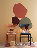 Two chairs in front of patches of colour on wall in warm shades