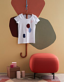 Painted T shirt and pouffe against wall with patches of colour