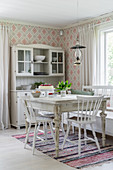 Antique, white-painted dresser and patterned wallpaper in dining area