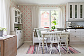 Antique, white-painted furniture, patterned wallpaper and rag rug in dining area
