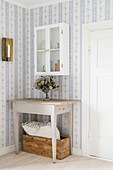 Old table and wall-mounted cabinet on landing with pretty wallpaper