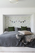 Double bed with head in niche with patterned wallpaper on back wall