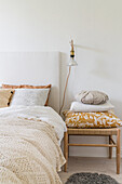 Double bed with crocheted bedspread, wall-mounted lamp and stool with cushions