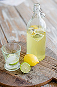 Bottle of lemonade, glass, lemon and lime on wooden board