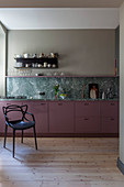 Black chair next to kitchen counter with berry-coloured cabinets