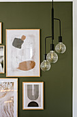 Pendant lamp in front of modern arrangement of pictures on green wall