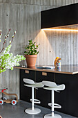 Modern kitchen counter with white bar stools and exposed concrete wall