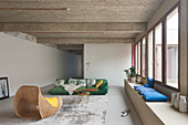 Open-plan living room with exposed concrete ceiling, green sofa and colorful cushions