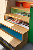 Wooden staircase with brightly colored risers and shelves and stacks of books