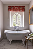 A freestanding bathtub, a Roman blind and leaded glass windows in a bathroom